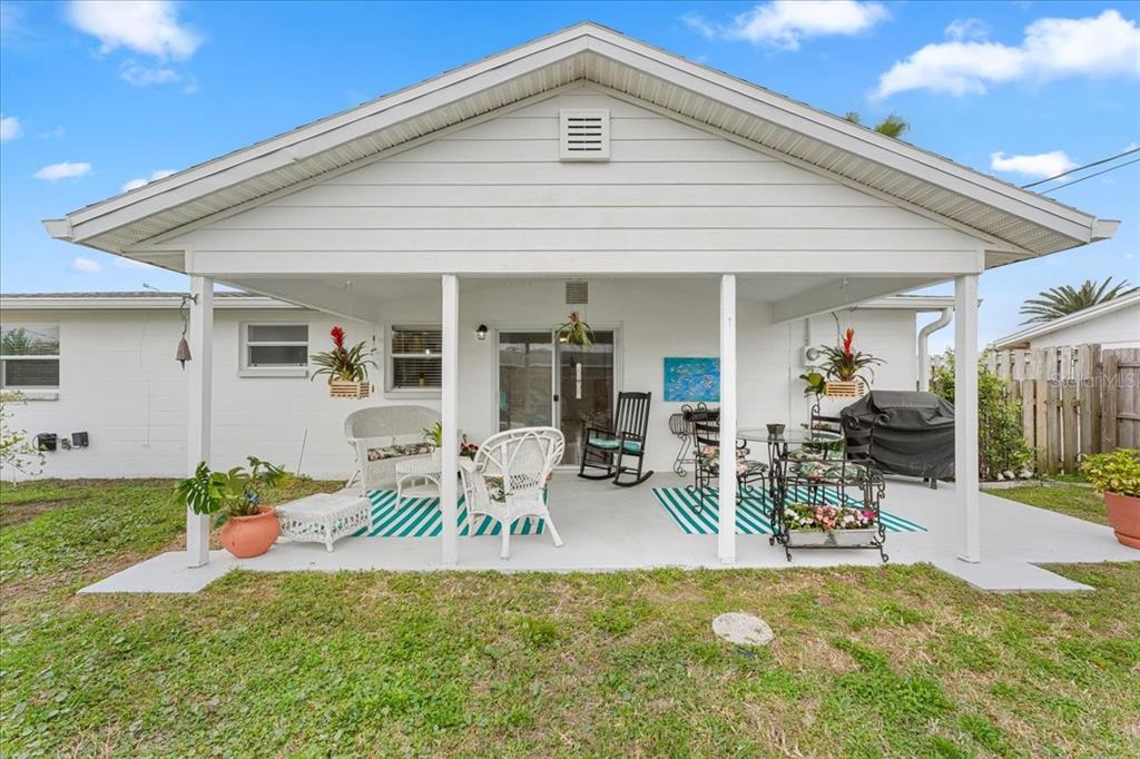 A covered patio with white furniture, a grill, and a striped rug overlooks a grassy yard — 3731 ELMWOOD DRIVE, HOLIDAY, FL