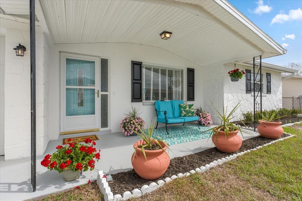 A covered front porch features a teal bench, potted plants, and a white exterior wall — 3731 ELMWOOD DRIVE, HOLIDAY, FL