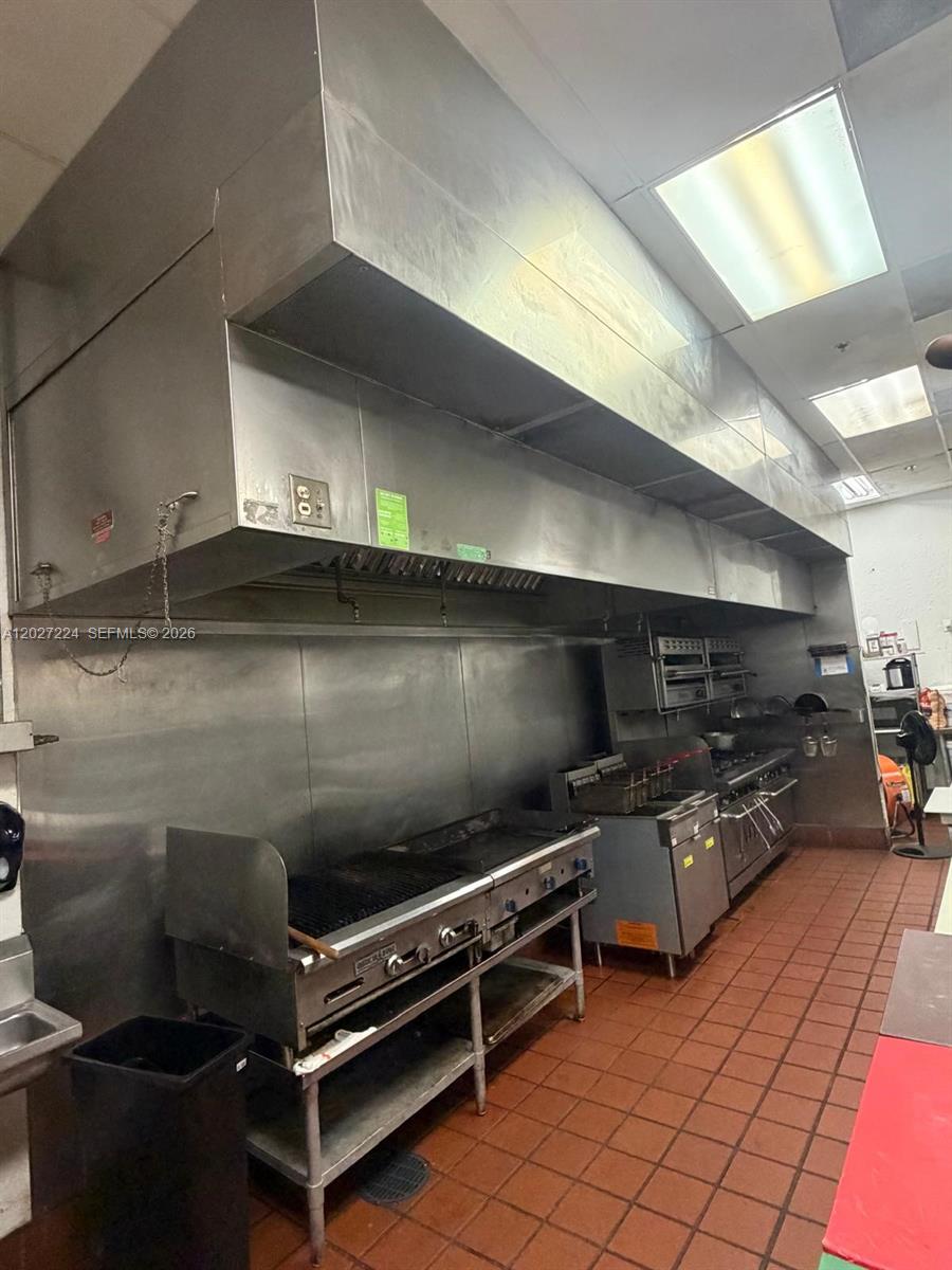 A commercial kitchen features stainless steel appliances, a large ventilation hood, and red tiled flooring — Confidential, Doral FL 33178, DORAL, FL