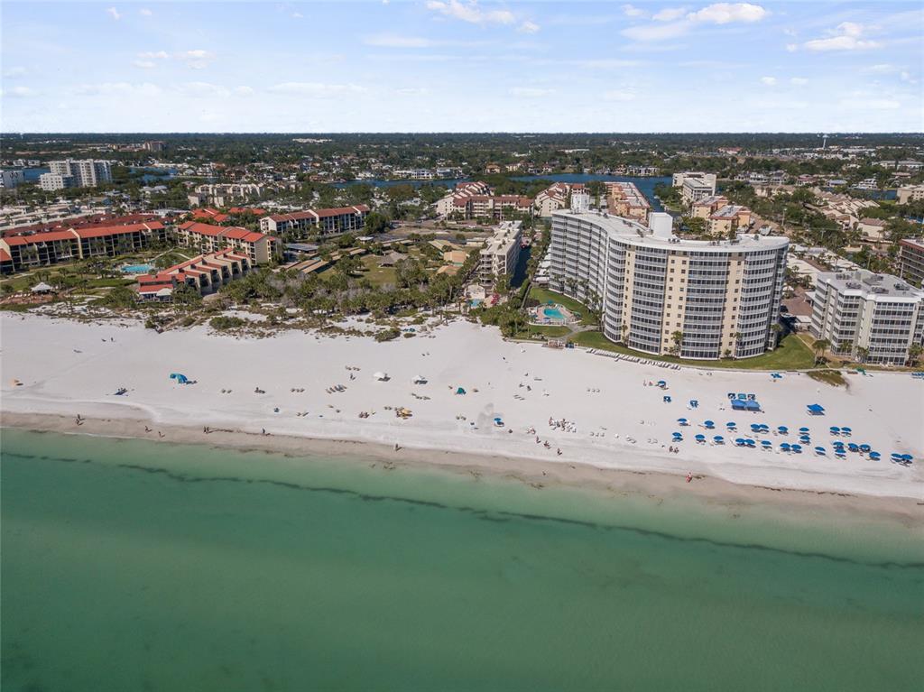 An aerial view of a sandy beach with a large curved hotel and surrounding buildings — 6266 MIDNIGHT PASS ROAD UNIT 404, SARASOTA, FL