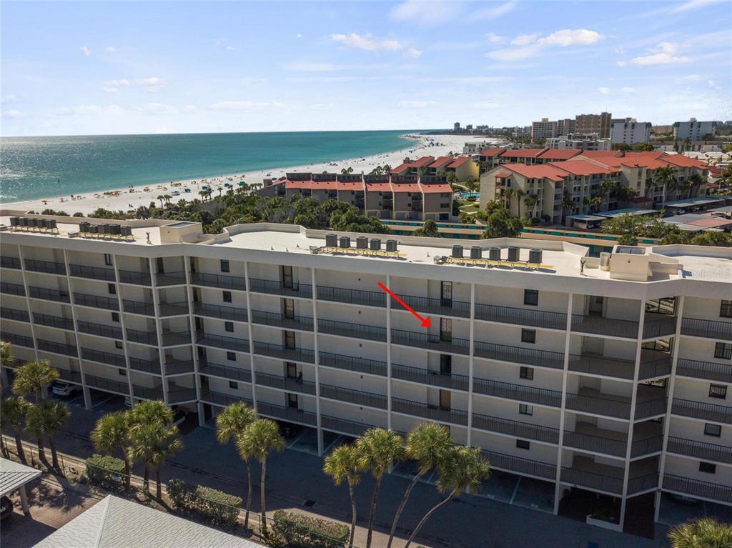 An aerial view of a multi-story beachfront condominium building with a red arrow indicating a unit — 6266 MIDNIGHT PASS ROAD UNIT 404, SARASOTA, FL