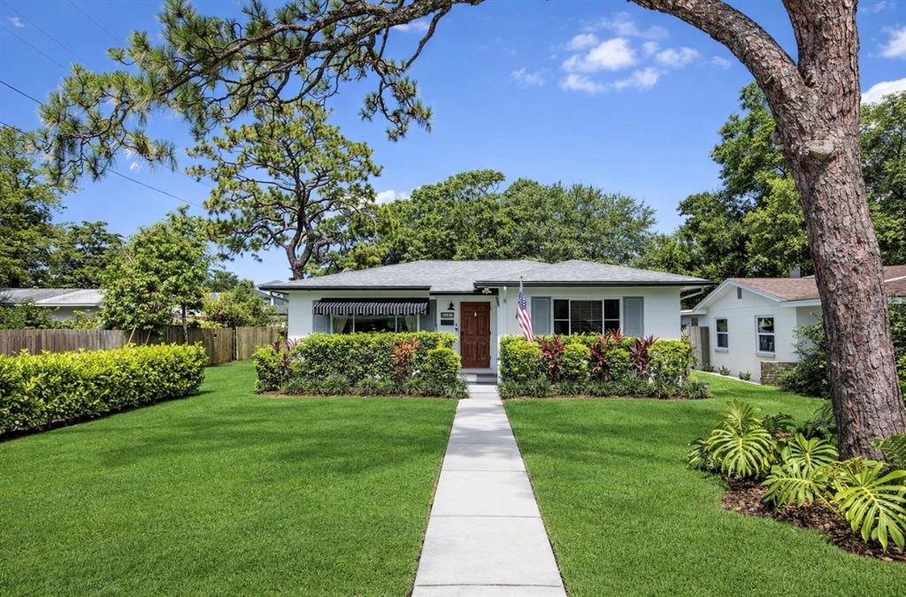 A white single-story house with a front lawn, sidewalk, and mature trees under a blue sky — 4020 QUEEN STREET N, ST PETERSBURG, FL