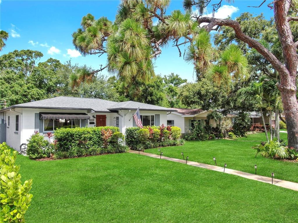 A single-story white house with a striped awning and an American flag on the lawn — 4020 QUEEN STREET N, ST PETERSBURG, FL