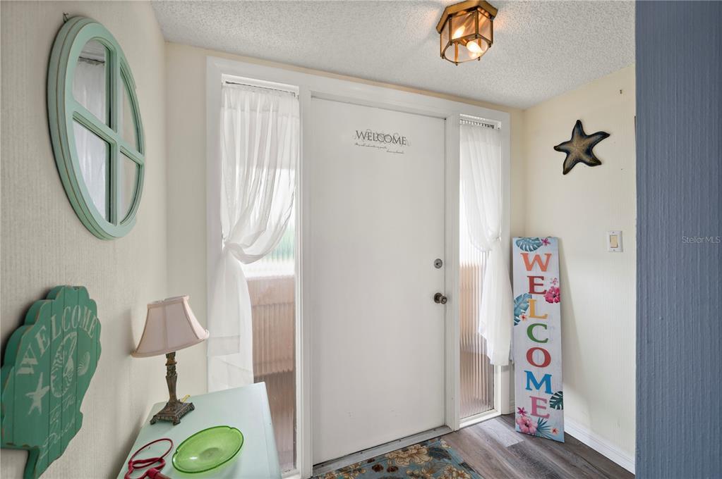 An entryway features a white front door, a welcome sign, and coastal-themed wall decor — 1080 BAL HARBOR BOULEVARD UNIT 9D, PUNTA GORDA, FL