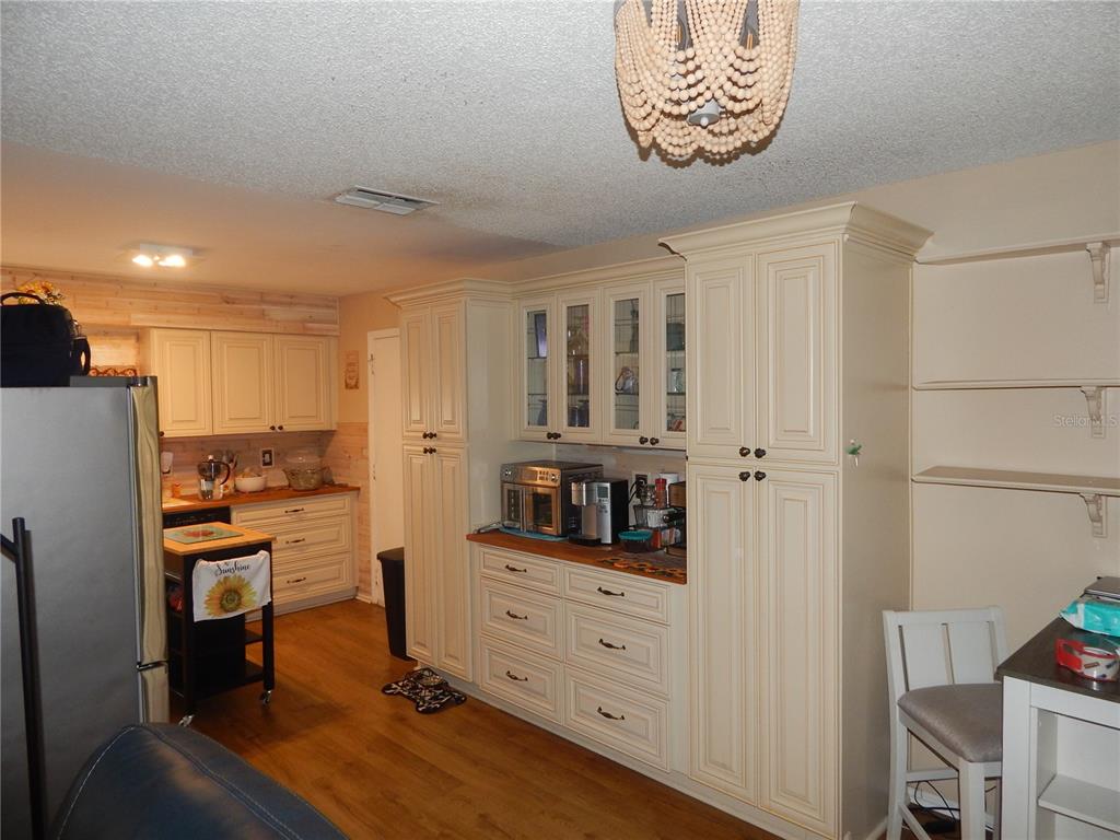 A kitchen features cream-colored cabinetry, wood-look flooring, a beaded chandelier, and a small rolling island — 5517 WESTBROOK DRIVE, ORLANDO, FL