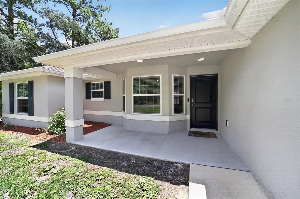 A gray house exterior features a covered concrete porch, a black front door, and windows — 14535 SW 68TH TERRACE, OCALA, FL