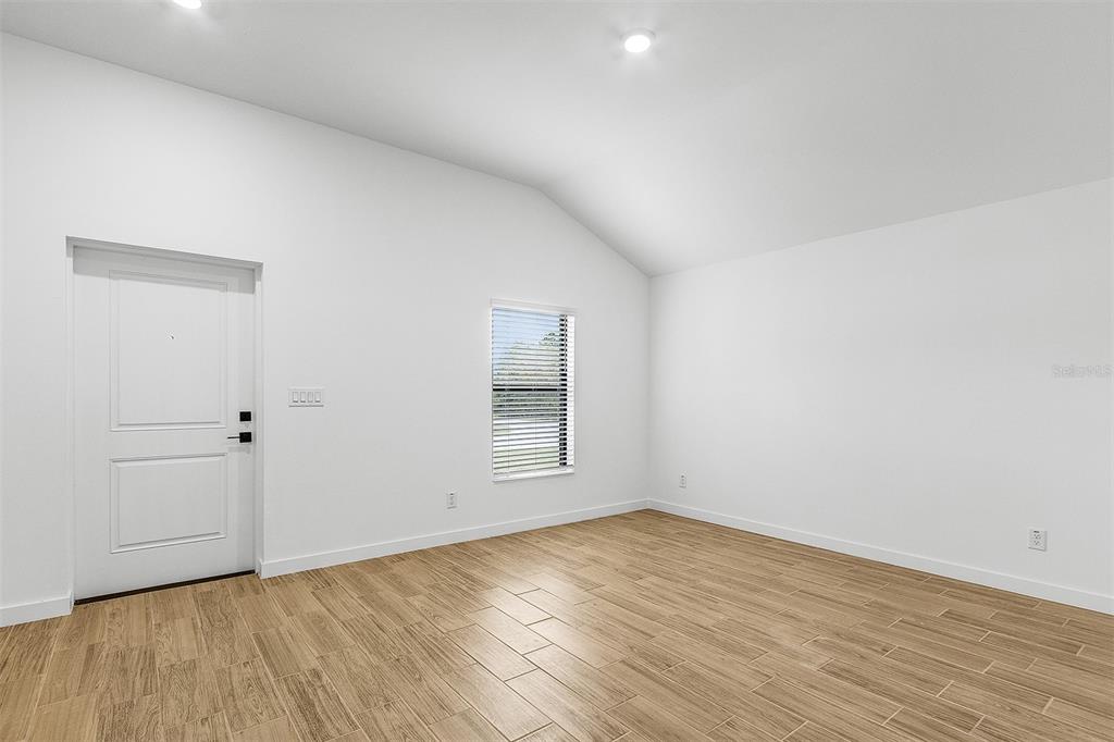 An empty room with white walls, a vaulted ceiling, a window, and wood-look tile flooring — 2791 SNUG STREET, NORTH PORT, FL
