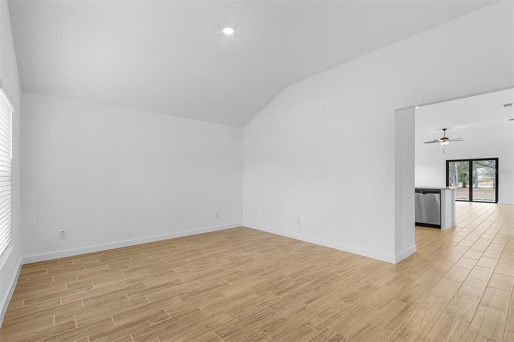 An empty room with light wood-look tile flooring and a vaulted ceiling leads to a kitchen — 2791 SNUG STREET, NORTH PORT, FL