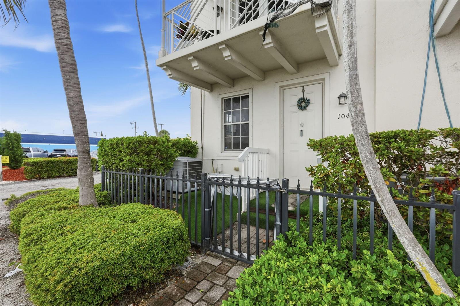 A white building exterior features a front door numbered 104, a small balcony, and landscaping — 310 N Dixie Highway # 104, FL 33460, FL