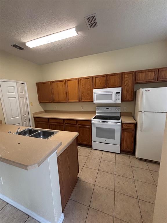 A kitchen features wood cabinets, white appliances, a tiled floor, and a peninsula with sink — 2417 TEMPLE GROVE LANE, KISSIMMEE, FL
