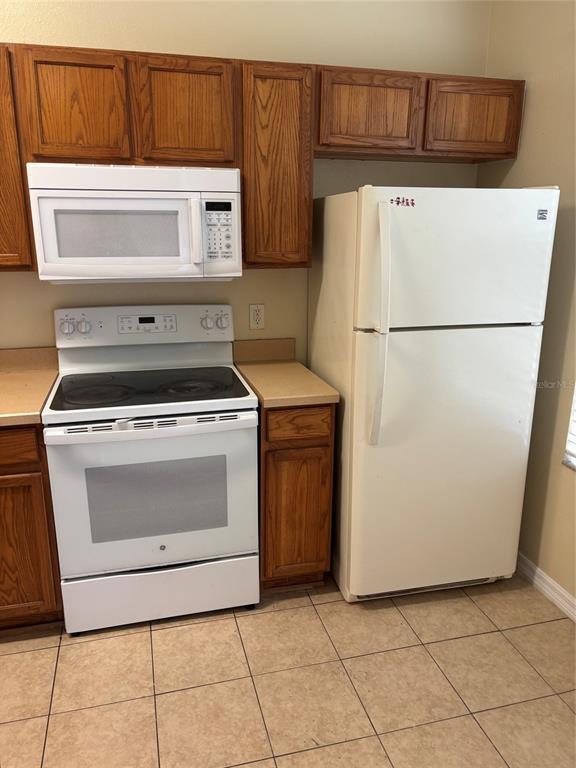 A kitchen features wood cabinets, white appliances, and tan tile flooring — 2417 TEMPLE GROVE LANE, KISSIMMEE, FL