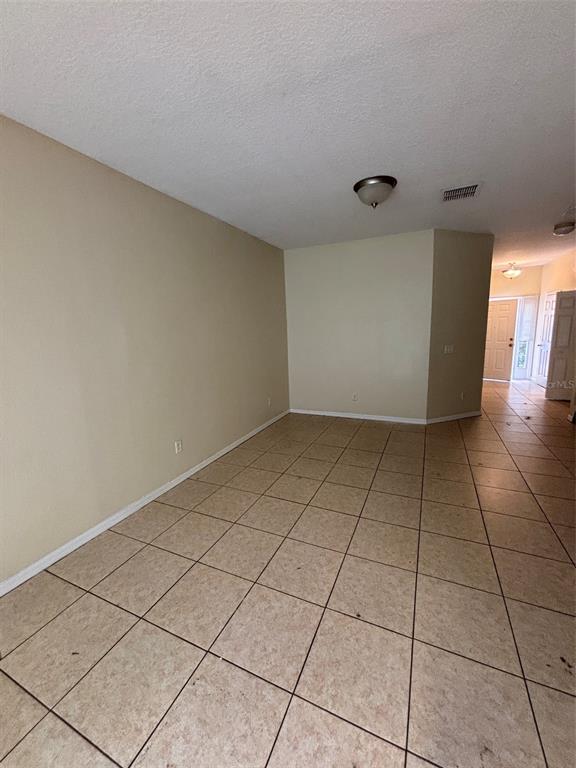 An empty room with beige walls and tan tile flooring leads to an entryway — 2417 TEMPLE GROVE LANE, KISSIMMEE, FL
