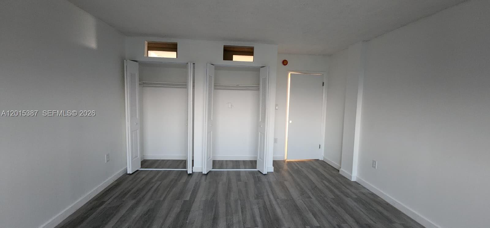 A room with gray wood-look flooring, two open closets, and a closed white door — 6930 Miami Gardens Dr # 512A, Hialeah FL 33015, HIALEAH, FL