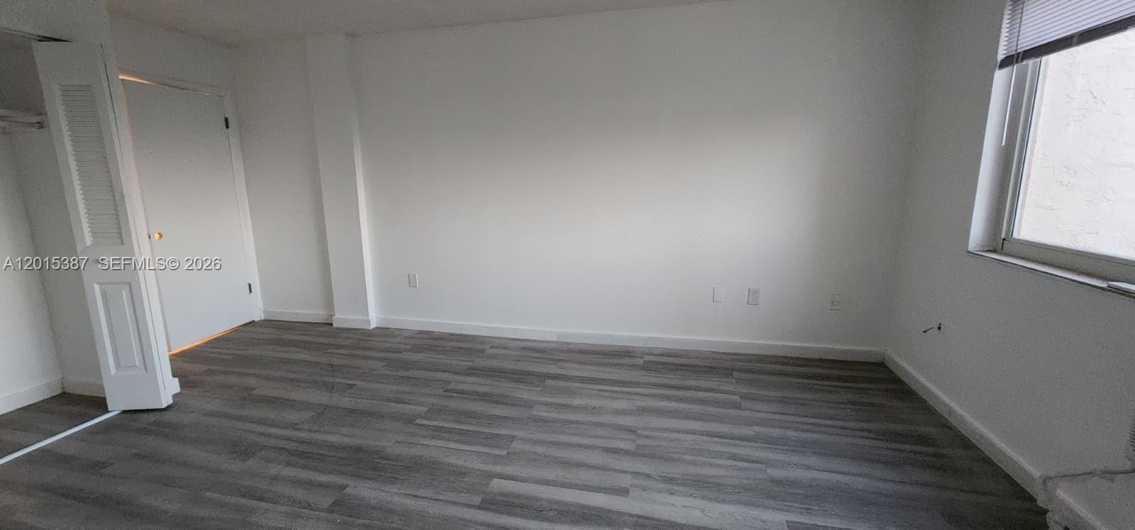 An empty bedroom features white walls, gray wood-look flooring, a closet, and a window — 6930 Miami Gardens Dr # 512A, Hialeah FL 33015, HIALEAH, FL