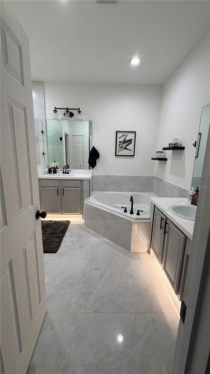 A modern bathroom features a corner soaking tub, double vanity, and light gray marble tile flooring — 14539 SAINT GEORGES HILL DRIVE, ORLANDO, FL