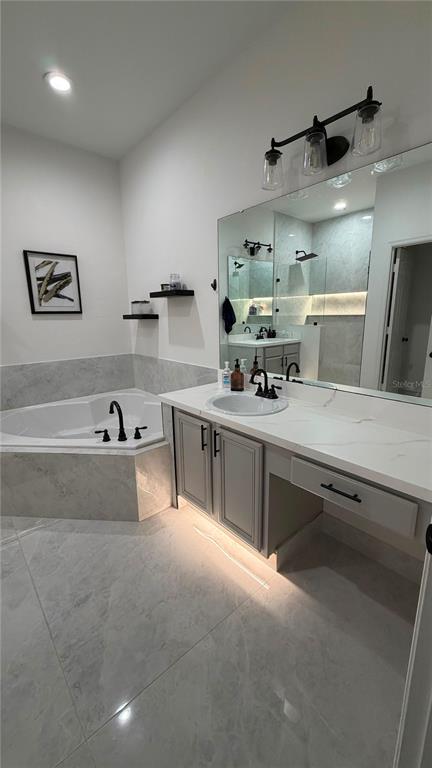 A modern bathroom features a corner soaking tub, a vanity with marble countertops, and lighting — 14539 SAINT GEORGES HILL DRIVE, ORLANDO, FL