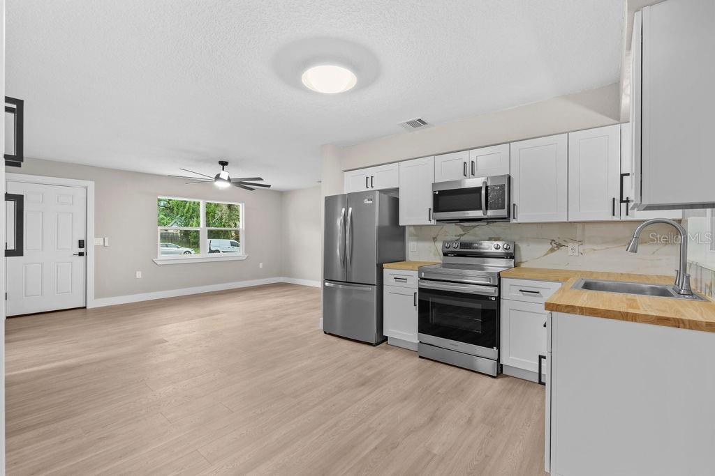 A kitchen with white cabinets, stainless steel appliances, wood countertops, and a sliding glass door — 5399 MUSTANG WAY, ORLANDO, FL