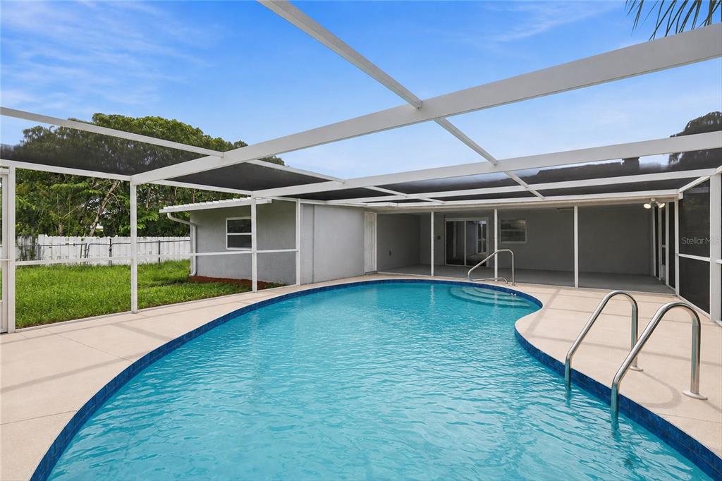 A swimming pool with a metal-framed screen enclosure sits behind a house with gray siding — 131 DEGAS DRIVE, NOKOMIS, FL