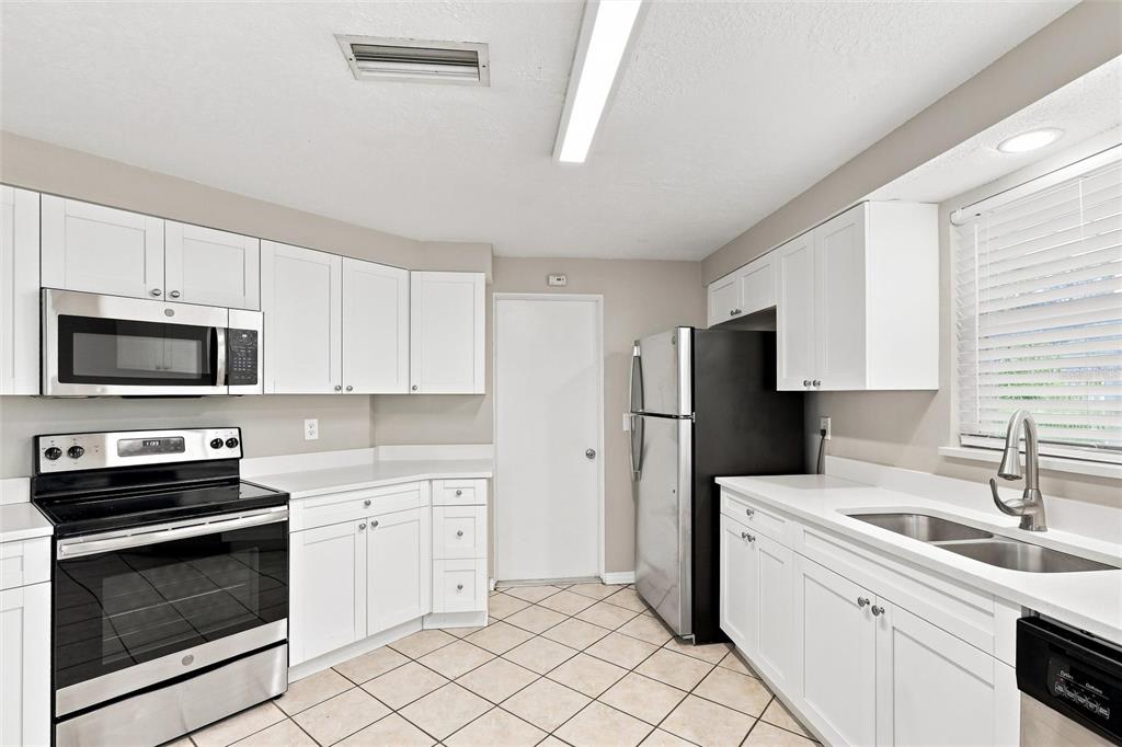 A kitchen features white cabinets, stainless steel appliances, white countertops, and light-colored tile flooring — 131 DEGAS DRIVE, NOKOMIS, FL