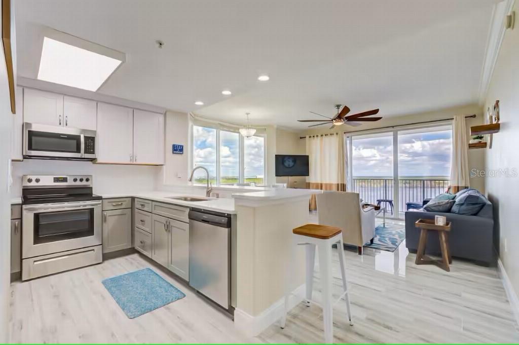 A kitchen with white cabinets and stainless steel appliances opens to a living area with views — 13415 BLUE HERON BEACH DRIVE UNIT 1201, ORLANDO, FL