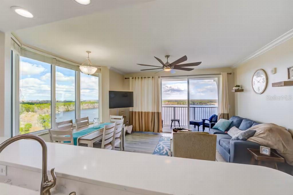 A bright living and dining area with water views, a ceiling fan, and blue furniture — 13415 BLUE HERON BEACH DRIVE UNIT 1201, ORLANDO, FL