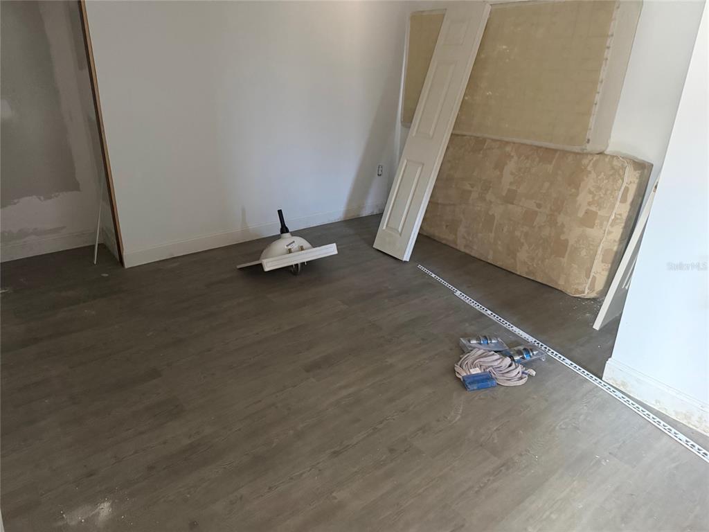 An unfinished room features gray wood-look flooring, a detached sink basin, and construction materials — 2432 CHASE AVENUE, SANFORD, FL