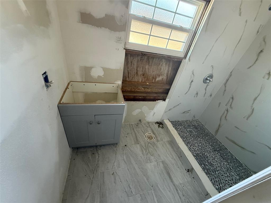 A bathroom under renovation features a gray vanity, tiled floor, and a walk-in shower — 2432 CHASE AVENUE, SANFORD, FL