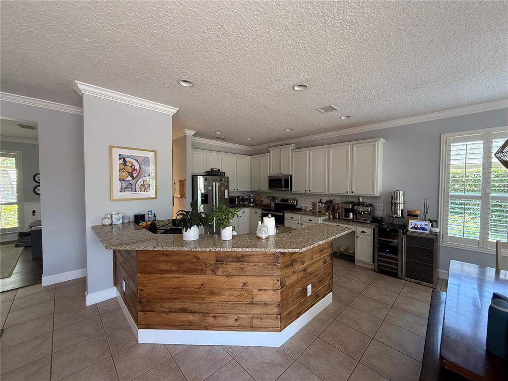 A kitchen features a wood-paneled peninsula, granite countertops, white cabinets, and tile flooring — 3425 TURNINGWIND LANE, WINTER GARDEN, FL