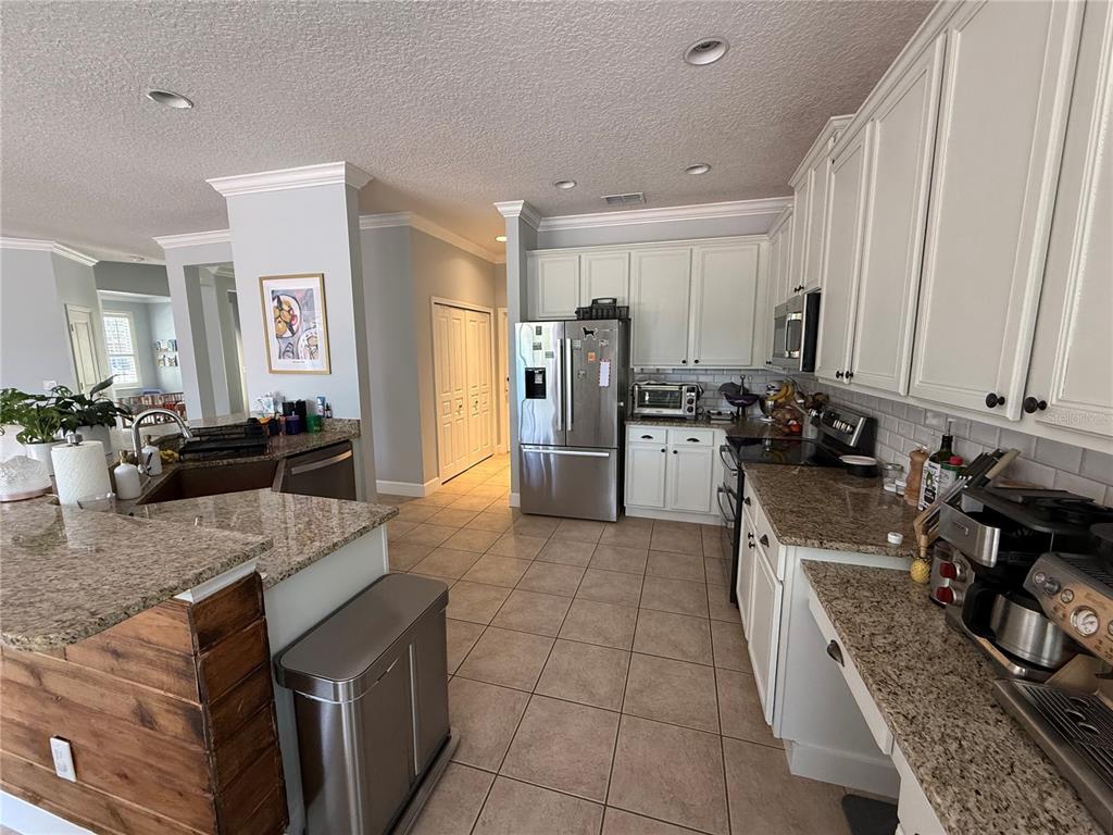 A kitchen with white cabinets, granite countertops, stainless steel appliances, and tile flooring — 3425 TURNINGWIND LANE, WINTER GARDEN, FL