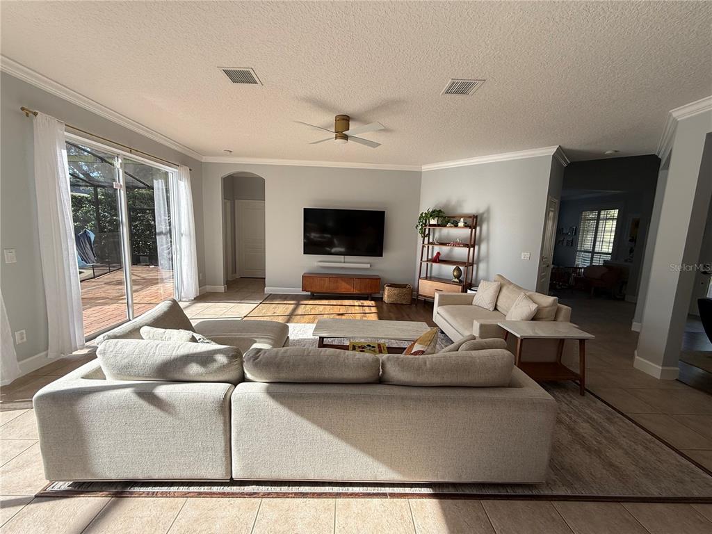 A living room features a large sectional sofa, a wall-mounted television, and sliding glass doors — 3425 TURNINGWIND LANE, WINTER GARDEN, FL