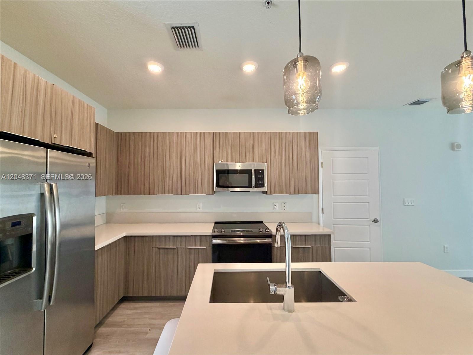 A modern kitchen features wood-grain cabinets, stainless steel appliances, and a central island with sink — 4740 NW 84th Ct # 33, Doral FL 33166, DORAL, FL