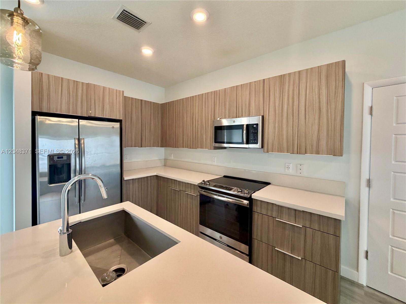 A modern kitchen features wood-grain cabinets, stainless steel appliances, and a white quartz island — 4740 NW 84th Ct # 33, Doral FL 33166, DORAL, FL