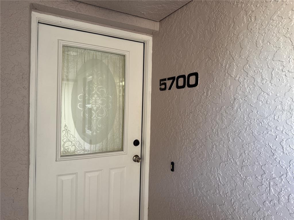 A white front door with a decorative glass insert is next to the number 5700 — 5700 SHEFFIELD GREENE CIRCLE UNIT 87, SARASOTA, FL
