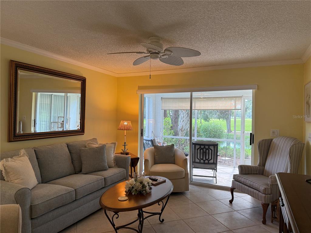 A living room features a grey sofa, an oval coffee table, and a sliding glass door — 5700 SHEFFIELD GREENE CIRCLE UNIT 87, SARASOTA, FL