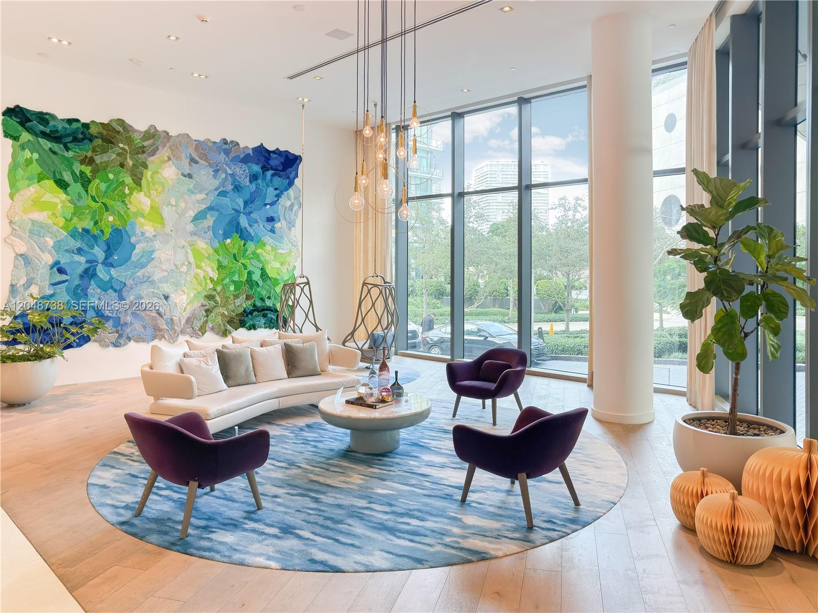 A modern lounge features a curved sofa, purple armchairs, a large wall tapestry, and floor-to-ceiling windows — 650 NE 32nd St # 802, Miami FL 33137, MIAMI, FL