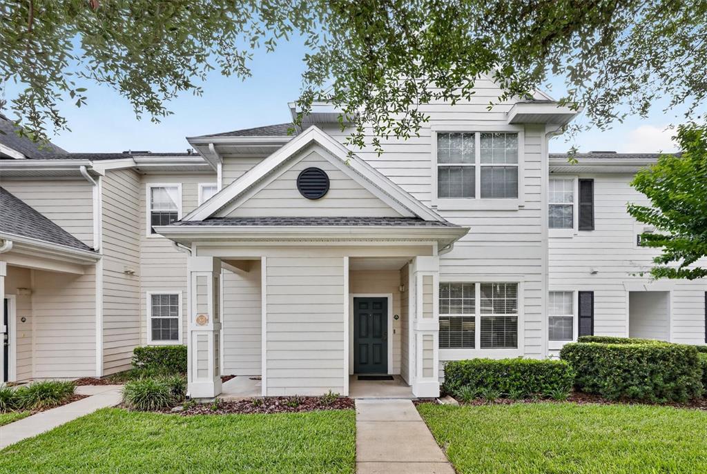 A two-story townhouse with beige horizontal siding, a covered entryway, and a small front lawn — 1300 EASTERN PECAN PLACE UNIT 102, WINTER GARDEN, FL