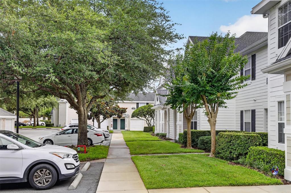 A white multi-story residential building with a sidewalk, green lawn, and parked cars — 1300 EASTERN PECAN PLACE UNIT 102, WINTER GARDEN, FL