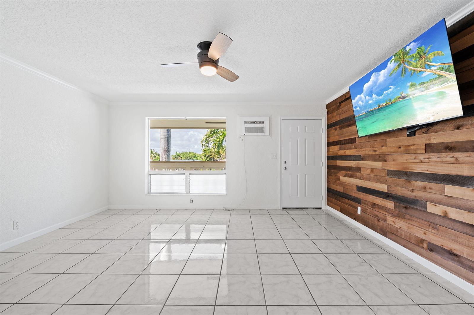 A living room with a wood-paneled accent wall, tile flooring, and an adjacent kitchen — 1780 SE 4th Street, Pompano Beach FL 33060, POMPANO BEACH, FL