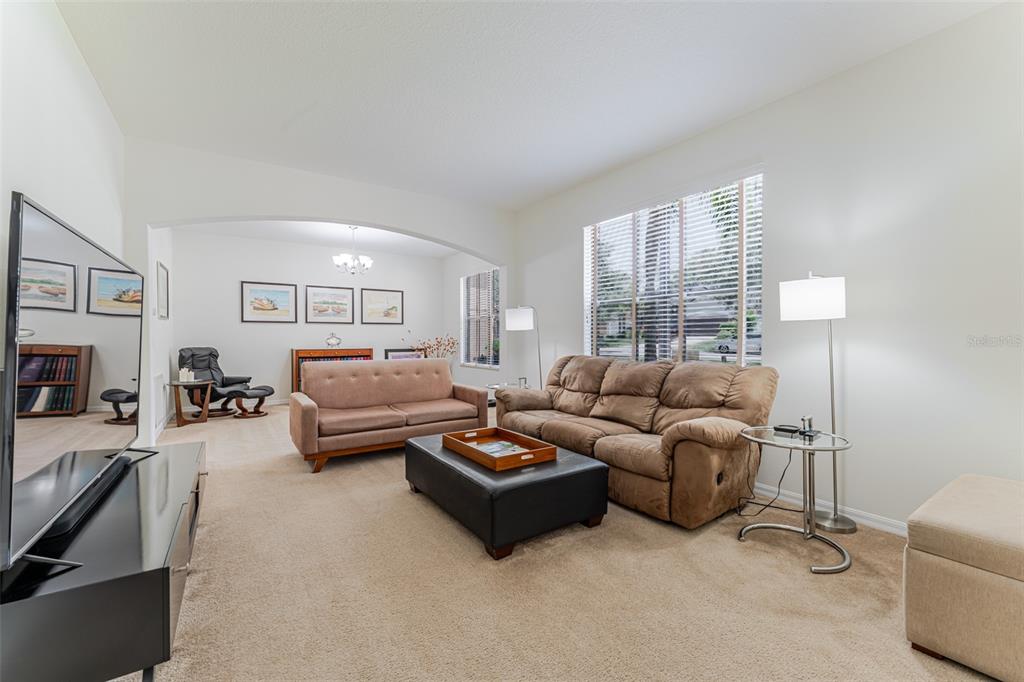 A living room features a brown sofa, a black ottoman, and a television on a stand — 1778 WATERSIDE OAKS DRIVE, ORANGE CITY, FL