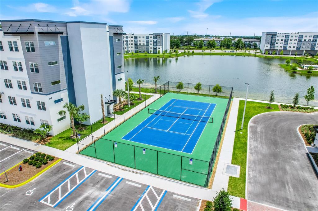 An aerial view shows a blue tennis court next to a large apartment building and pond — 5579 MILLENIA PARK BOULEVARD UNIT 508, ORLANDO, FL