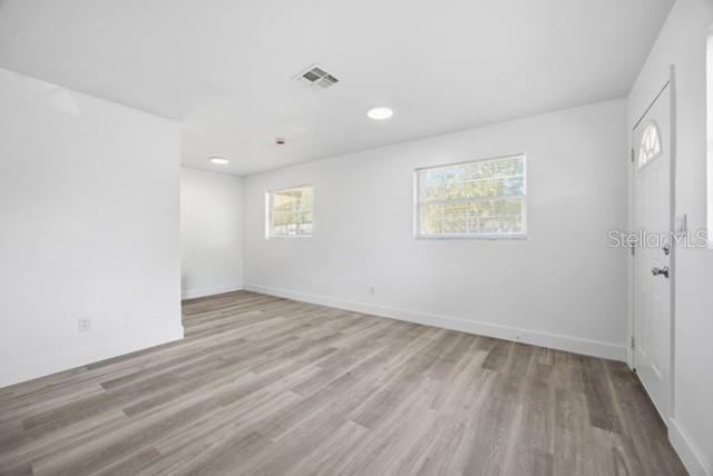An empty room with white walls, light wood-look flooring, two windows, and a white door — 1105 LINCOLN TERRACE, WINTER GARDEN, FL