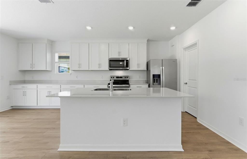A modern kitchen features white cabinetry, stainless steel appliances, and a large central island — 1090 SILVERLAKE BOULEVARD, LAKE ALFRED, FL