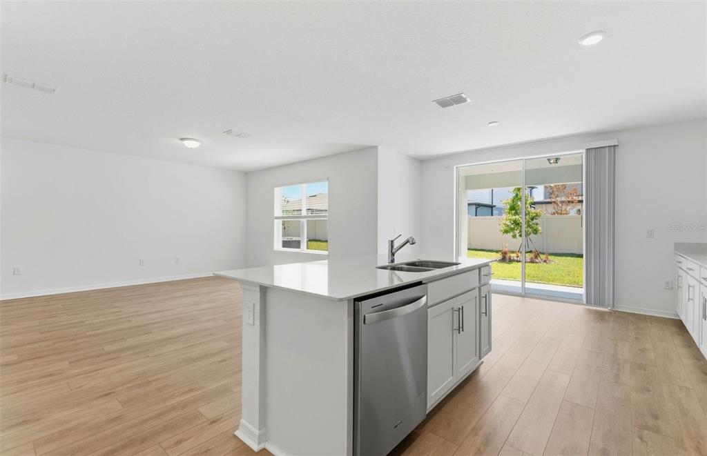 A kitchen island with a stainless steel dishwasher faces a living area with wood flooring — 1090 SILVERLAKE BOULEVARD, LAKE ALFRED, FL