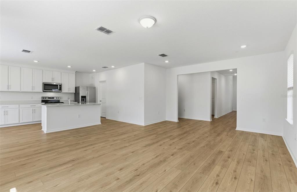 A bright, open-concept kitchen and living area featuring white cabinets and light wood flooring — 1090 SILVERLAKE BOULEVARD, LAKE ALFRED, FL