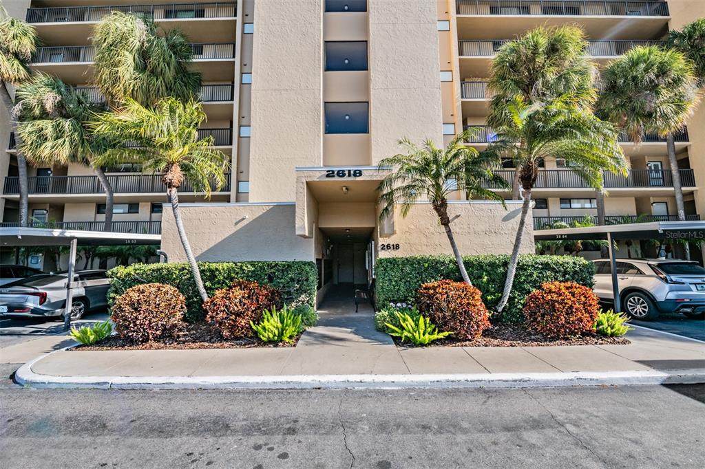 The exterior of a multi-story residential building features palm trees and a covered entrance — 2618 COVE CAY DRIVE UNIT 204, CLEARWATER, FL