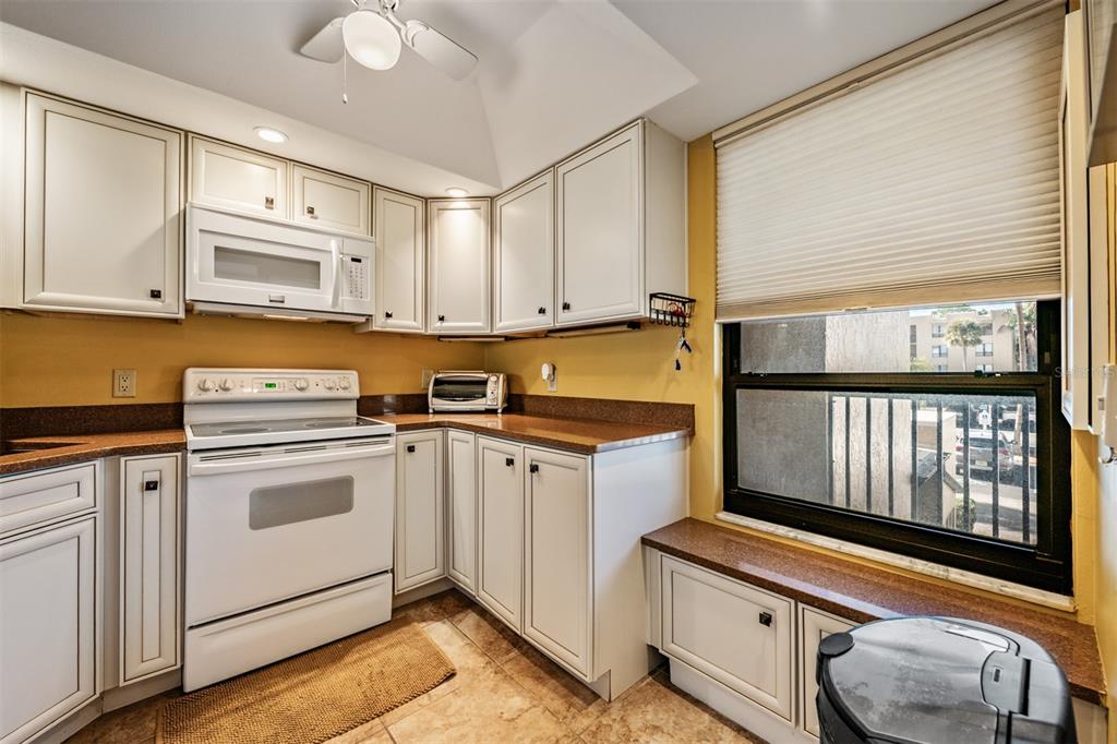 A kitchen with white cabinets, brown countertops, a white stove, and a window with blinds — 2618 COVE CAY DRIVE UNIT 204, CLEARWATER, FL