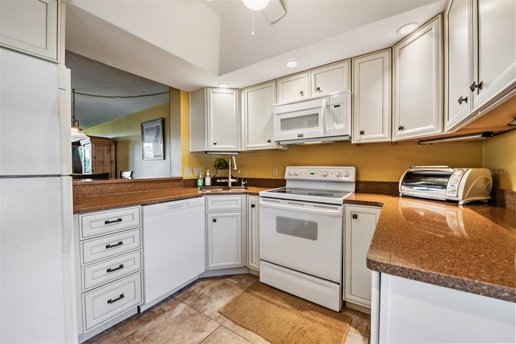 A kitchen features white cabinets, granite countertops, white appliances, and light-colored floor tiles — 2618 COVE CAY DRIVE UNIT 204, CLEARWATER, FL