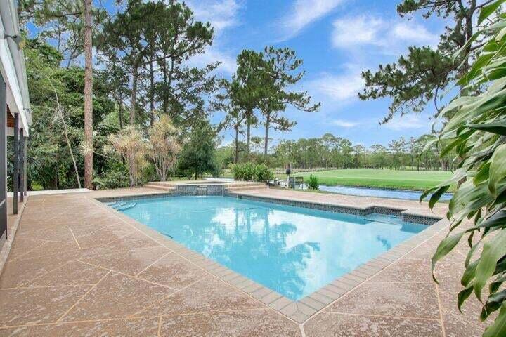 A rectangular swimming pool with a spillover spa sits on a paved patio overlooking greenery — 1328 SE Colony Way, Jupiter FL 33478, JUPITER, FL