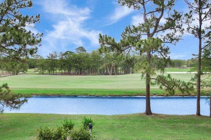 A view of a golf course fairway across a pond with pine trees in the foreground — 1328 SE Colony Way, Jupiter FL 33478, JUPITER, FL
