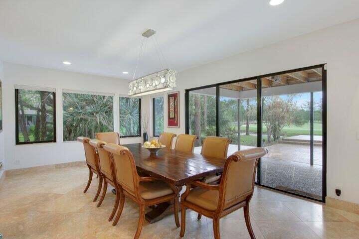 A dining room with a wooden table, tan chairs, a chandelier, and large glass sliding doors — 1328 SE Colony Way, Jupiter FL 33478, JUPITER, FL
